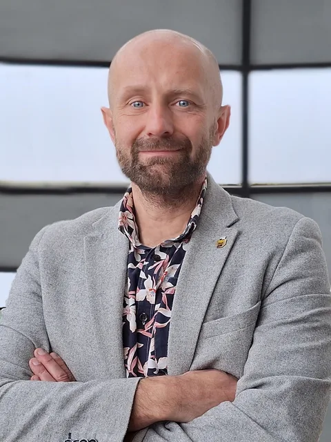 Marcin Świtoniak Marcin Świtoniak w szarej marynarce, prelegent pokazu maszyn Czajkowski.