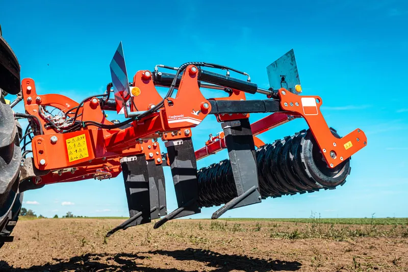 Czerwony głębosz Czajkowski VT 300 z zębami roboczymi i wałem, podłączony do ciągnika na polu.